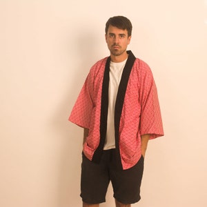 Peut inclure: Une personne portant un kimono rouge et noir à motifs avec un col noir et un t-shirt blanc en dessous. La personne porte un short noir.