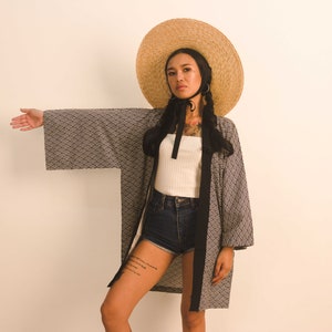May include: A woman wearing a black and white patterned kimono with a wide-brimmed straw hat and black ribbon. She is wearing denim shorts and a white tank top.