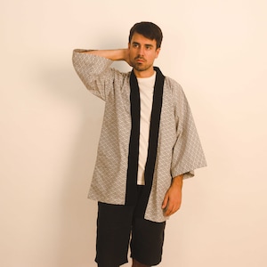 May include: A man wearing a gray and white patterned kimono with black trim. He is wearing a white t-shirt underneath and black shorts.