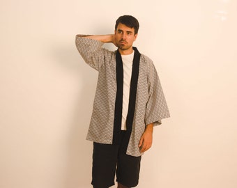 May include: A man wearing a gray and white patterned kimono with black trim. He is wearing a white t-shirt underneath and black shorts.