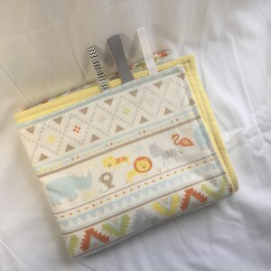 K&ouml;nnte beinhalten: Eine gelbe und wei&szlig;e Babydecke mit geometrischem Muster und Tierillustrationen. Die Decke hat einen gelben Rand und ist in der H&auml;lfte gefaltet.