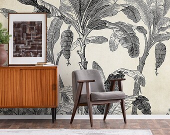 May include: A room interior featuring a mid-century modern style. A wooden cabinet with a framed artwork and a small plant sits next to a gray armchair. The wall is decorated with a black and white banana leaf wallpaper.