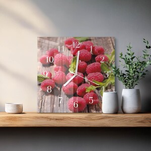 May include: Square wall clock with a close-up image of red raspberries on a wooden surface. The clock face has white numerals and hands. The clock is a decorative item, showing the time. The clock is a decorative item.