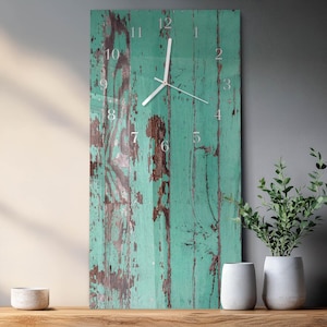 May include: A rectangular wall clock with a distressed teal wood-look face. The clock features silver-colored hands and numerals. The wood has brown patches where the paint has chipped away, giving it a rustic appearance. The clock is a decorative home decor item.