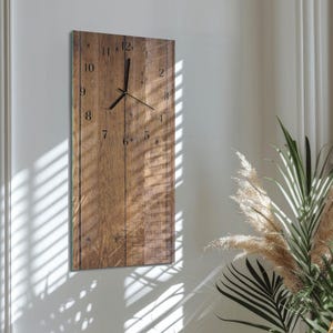 Può includere: Un orologio da parete rettangolare con un design a doghe di legno. Il quadrante presenta numeri e lancette neri. L'orologio è montato su una parete bianca, con luce naturale e ombre che aggiungono profondità alla scena. L'orologio misura circa 30 cm di larghezza e 76 cm di altezza.