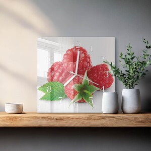 May include: Square wall clock with a close-up image of ripe raspberries. The clock face has white numerals and hands, set against a background of red fruit and green leaves. A decorative item for the kitchen or dining room, measuring approximately 30 cm x 30 cm.