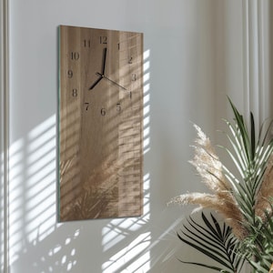 May include: A rectangular wooden wall clock with black numerals and hands. The clock has a natural wood grain finish and is mounted on a white wall. The clock's design is minimalist and modern, suitable for home decor.