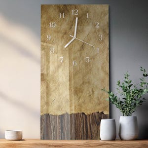 May include: A rectangular wall clock with a vintage paper design. The clock face features white numerals and hands against a textured, tan background. The bottom portion has a wood-grain appearance. The clock is displayed on a wooden surface.