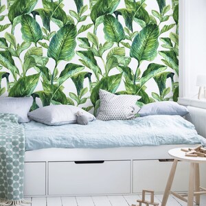 Può includere: Un letto bianco con un copriletto blu chiaro e carta da parati con motivi di foglie verdi. Il letto ha tre cassetti bianchi sotto. Uno sgabello di legno piccolo si trova accanto al letto con blocchi di legno sparsi sul pavimento.