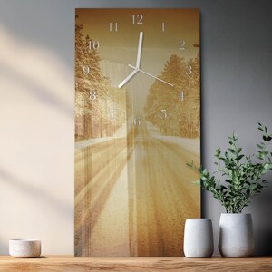 May include: Rectangular wall clock featuring a sepia-toned image of a road through a forest. The clock face has silver numerals and hands. The image has a vintage aesthetic, with a warm, golden colour palette.