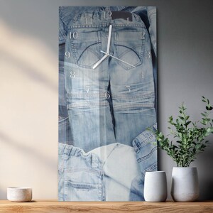 May include: A rectangular wall clock with a denim jeans design. The clock face features white numerals and hands, with the jeans' back pockets and seams visible. The clock is a decorative item for a home.