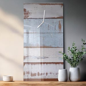 May include: A rectangular wall clock with a distressed wood design in shades of white and light blue. The clock face features silver numerals and hands. The clock is displayed with two white vases and a small bowl.