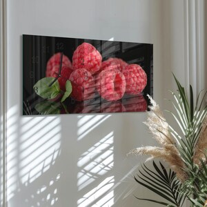 May include: A rectangular wall clock featuring a close-up of fresh red raspberries with green leaves. The clock face displays the numbers 8, 9, 10, 11, and 12. The background is dark, with light and shadow from a window.