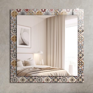 Könnte beinhalten: Ein dekorativer Spiegel mit einem gemusterten Rahmen. Der Rahmen zeigt ein geometrisches Design in Rot-, Braun-, Gelb- und Grautönen. Der Spiegel spiegelt ein Schlafzimmer-Interieur mit einem Bett, Vorhängen und einer Lampe wider.