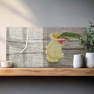 May include: A rectangular wall clock with a wooden background and a partially eaten apple. The clock face has white numbers and hands. The apple is yellow and red with a green leaf. The clock is on a wooden shelf.