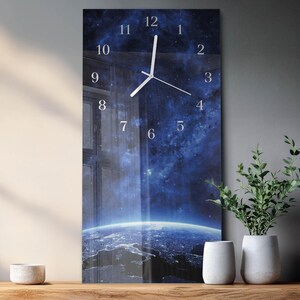 May include: A rectangular wall clock with a space-themed design. The clock face features a depiction of Earth from space, with a blue and white color scheme. White clock hands indicate the time. The clock is displayed on a wooden surface.