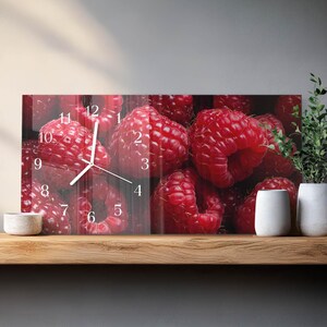 May include: A rectangular wall clock with a vibrant image of fresh red raspberries. The clock face features white hands and black numerals. The clock is displayed on a wooden shelf with decorative white vases and a small bowl.