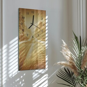 Könnte beinhalten: Eine rechteckige Wanduhr mit Landschaftsdesign. Das Zifferblatt hat schwarze Zeiger und Ziffern vor einem sepiafarbenen Bild einer Straße durch einen Wald. Die Uhr ist an einer weißen Wand befestigt.