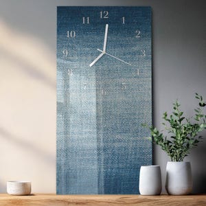 May include: A rectangular wall clock with a denim texture background. The clock face features white numerals and hands. The clock is approximately 12 inches tall and 6 inches wide.