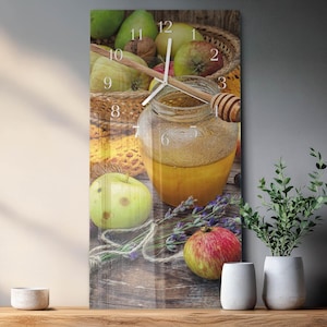 May include: A rectangular wall clock featuring a still life with a jar of honey, apples, and a honey dipper. The clock face has black numerals and hands. The background includes a basket of fruit and a sprig of lavender.
