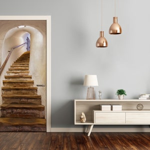 Può includere: Un adesivo per porta con un'immagine realistica di una scala in pietra che conduce a un soffitto a volta. La scala è in pietra grezza e ha un corrimano in legno. Il soffitto è bianco e ha un apparecchio di illuminazione al centro.