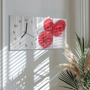 May include: A rectangular wall clock with a white background features black numerals and hands. The clock face displays a blurred image of red raspberries. The clock is mounted on a white wall.