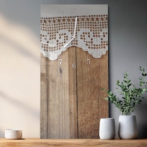 May include: A rectangular wall clock with a wooden background and a white lace design at the top. The clock face features silver numerals and hands. The clock is displayed on a wooden surface with decorative plants.