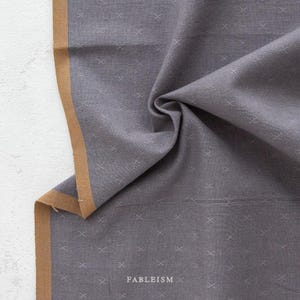 May include: Gray fabric with a subtle white crosshatch pattern and a brown border. The fabric is folded and the brand name "FABLEISM" is visible at the bottom.