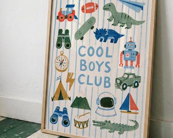 May include: A framed wall art print featuring a light blue striped background with the text COOL BOYS CLUB in the center. The print displays various illustrations including a train, football, skateboard, dinosaur, robot, truck, tent, and compass.