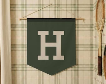 May include: A dark green pennant with a large white letter "H" hangs on a wall with plaid wallpaper. Two vintage tennis rackets are mounted on the wall. A cream-colored curtain is on the left.