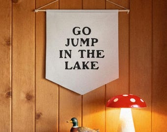 May include: A room with wood paneling, a green locker, and a white banner that reads "GO JUMP IN THE LAKE." A mushroom-shaped lamp with a red top and white spots sits on the locker. A decorative duck is also on the locker.