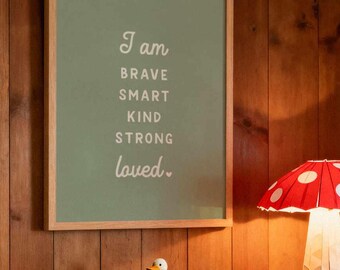 May include: A framed green print with the words "I am brave, smart, kind, strong, loved." is mounted on a wood-paneled wall. A red and white mushroom lamp sits on a green cabinet, next to a small white duck figurine.
