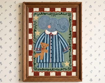 May include: A framed wall art print featuring a blue elephant wearing blue and white striped pajamas, holding a small brown teddy bear. The illustration is set against a sage green background with yellow stars, framed by a red and white checkered border.