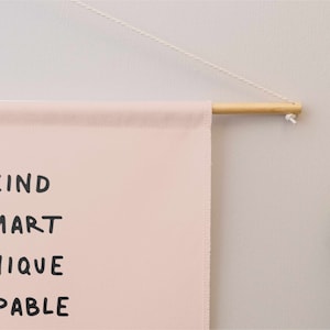May include: A pink canvas wall hanging with the words "KIND SMART UNIQUE CAPABLE" written in black.