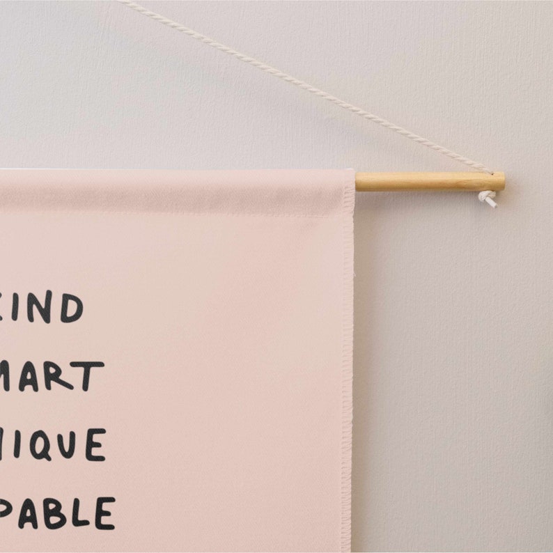 May include: A pink canvas wall hanging with the words "KIND SMART UNIQUE CAPABLE" written in black.