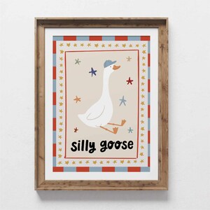 May include: A framed print featuring a whimsical illustration of a white goose wearing a blue cap, with the words "silly goose" in black. The artwork is surrounded by a red, white, and blue border with star accents, perfect for a nursery or child's room.