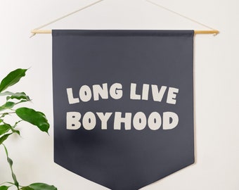 May include: A dark blue banner with white text that reads "Long Live Boyhood". The banner is hanging from a wooden dowel rod with white string.