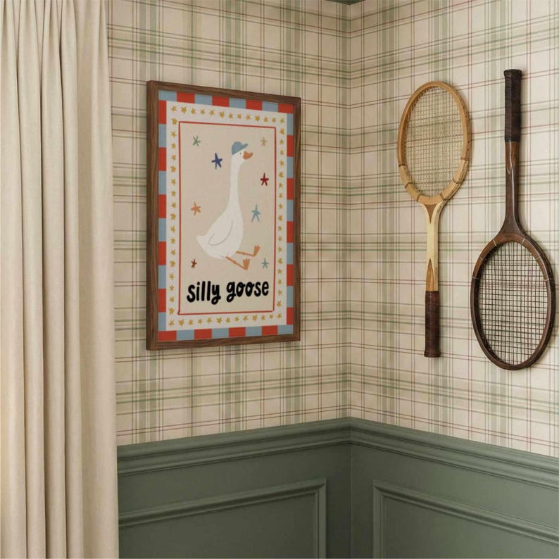 May include: A framed print with a cartoon goose wearing a hat and the words "silly goose". Two vintage wooden tennis rackets hang on a plaid wallpapered wall. A cream-colored curtain is on the left.