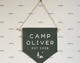 May include: A dark green banner with the text "CAMP OLIVER EST 2026" in white, along with a tree and tent graphic. The banner is suspended by a wooden dowel and string, against a white background with fish illustrations.