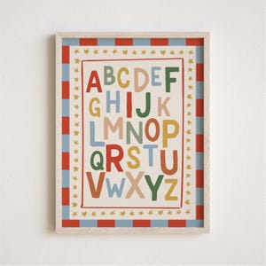 May include: A framed alphabet print with a cream background. The letters A through Z are in various colors. The frame has a red and blue striped border, with gold stars around the inner edge. The print is designed for children's rooms.