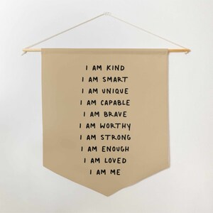 May include: A beige canvas wall hanging with the text "I am kind, I am smart, I am unique, I am capable, I am brave, I am worthy, I am strong, I am enough, I am loved, I am me" written in black.