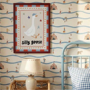 May include: A framed print featuring a whimsical illustration of a goose wearing a blue cap, with the words "silly goose" below. The frame has a red border with blue and white accents. The background is a circus-themed wallpaper.