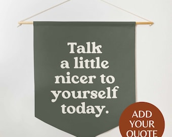 May include: A dark olive green fabric wall banner featuring the white text "Talk a little nicer to yourself today." The banner is suspended from a light-colored wooden dowel with a thin white string attached for hanging on a wall.