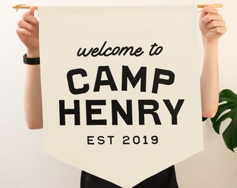 May include: A white canvas banner with black text that reads "welcome to CAMP HENRY EST 2019".