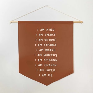May include: A brown felt banner with white text that reads "I am kind, I am smart, I am unique, I am capable, I am brave, I am worthy, I am strong, I am enough, I am loved, I am me."