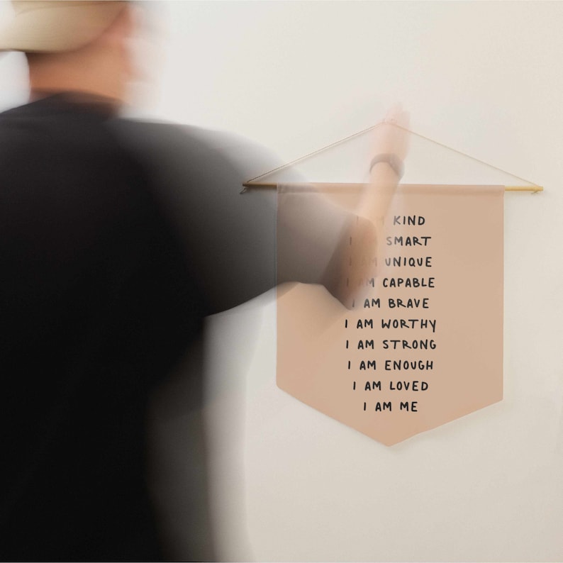 May include: A beige fabric banner with the text "KIND SMART UNIQUE I AM CAPABLE I AM BRAVE I AM WORTHY I AM STRONG I AM ENOUGH I AM LOVED I AM ME" written in black marker.