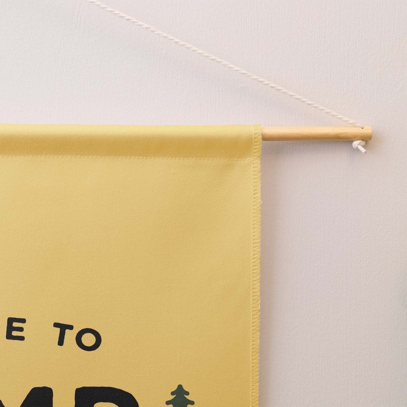Peut inclure: Une banni&egrave;re murale en tissu jaune avec le texte noir "E TO" et une petite ic&ocirc;ne de sapin vert. La banni&egrave;re est suspendue &agrave; une tige en bois clair par une fine cordelette blanche, formant un affichage simple pour une surface murale.
