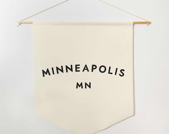 May include: A white canvas banner with black text that reads "MINNEAPOLIS MN" hanging from a wooden dowel rod.