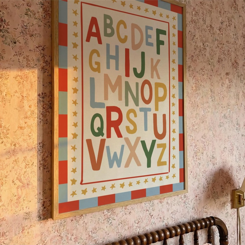 May include: A framed alphabet poster with colorful letters. The letters are in various colors, including red, green, and blue, against a cream background. The frame is a light wood color, and the poster is decorated with stars.