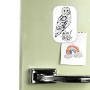Peut inclure: Un aimant rectangulaire avec une illustration détaillée en noir et blanc d'une chouette effraie perchée sur une souche d'arbre. L'aimant est affiché sur une porte de réfrigérateur vert clair, avec un petit dessin d'arc-en-ciel attaché en dessous.
